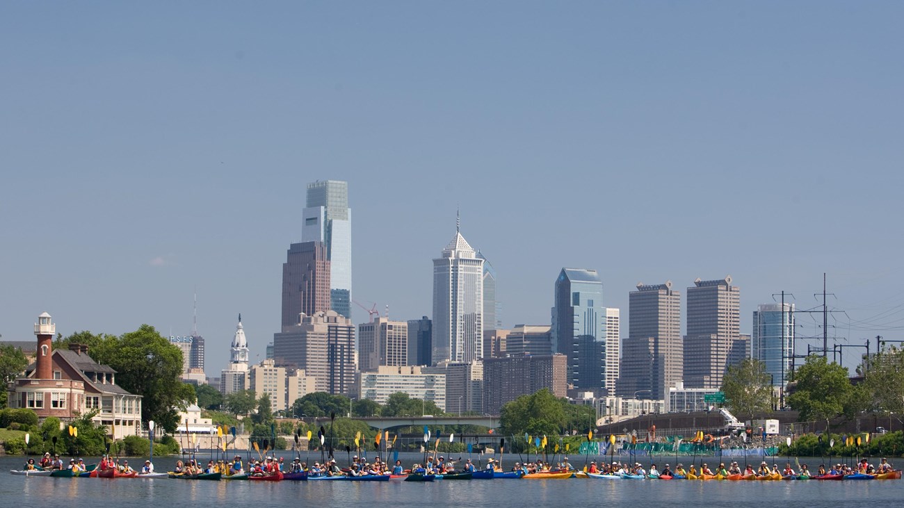 Row of kayakers lift their paddles in front of city skyline