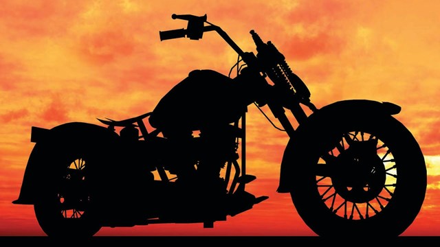 A black silhouette of a motorcycle stands in contrast to a bright orange and red sunset.