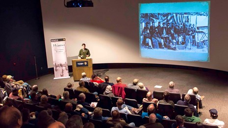 A park ranger presents a Winter Lecture program to a group of visitors in the theater.