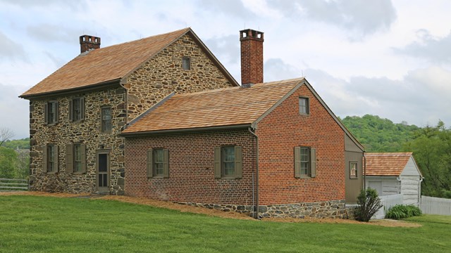 Historic brick and stone home surrounded by green grass and trees in the distance.