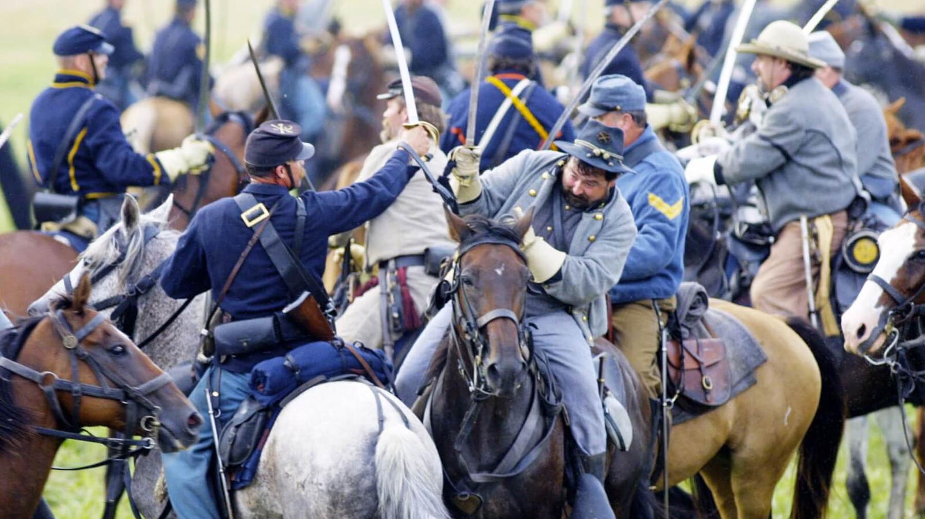A scene of Civil War cavalry soldiers reenacting a fight scene while on horseback.