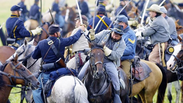 A scene of Civil War cavalry soldiers reenacting a fight scene while on horseback.