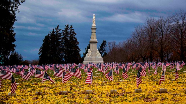 Yellow leaves on the ground and small U.S. flags fly over graves in the Soldiers' National Cemetery.