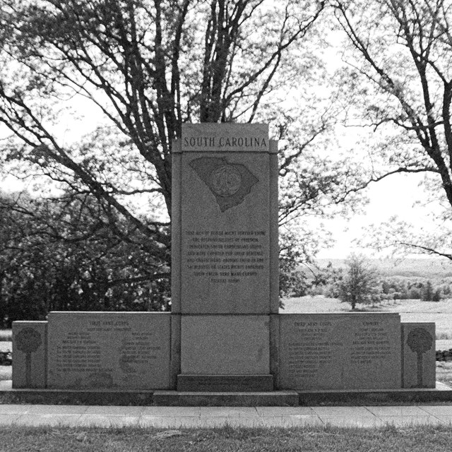A black and white photo of a granite monument with engraved text and a picture of South Carolina.