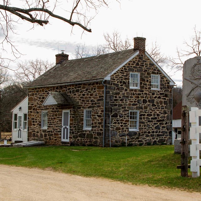 Student program about civilian caught in the crosshairs of battle. Image of stone house.