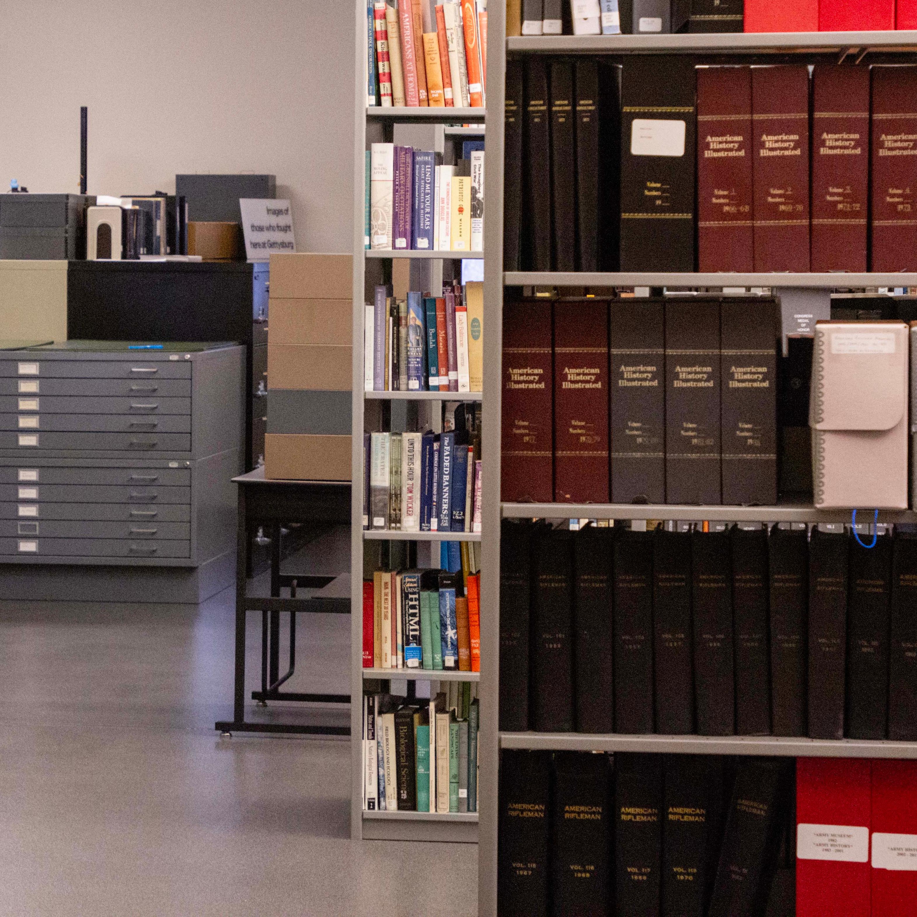 A scene from inside a library. Rows of grey metal bookshelves jut out from the right and continue.