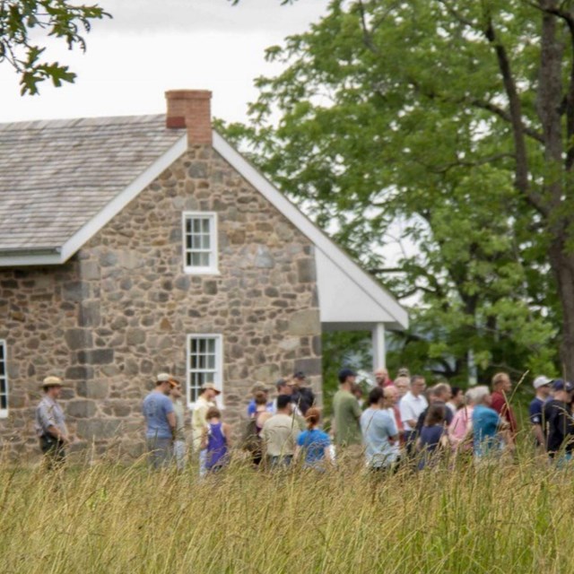 Ranger with a group of people near a stone house