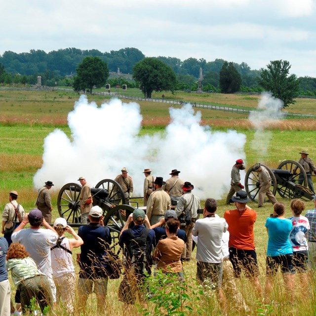 Confederate living historians demonstrate how to load and fire a cannon to a large group of visitors