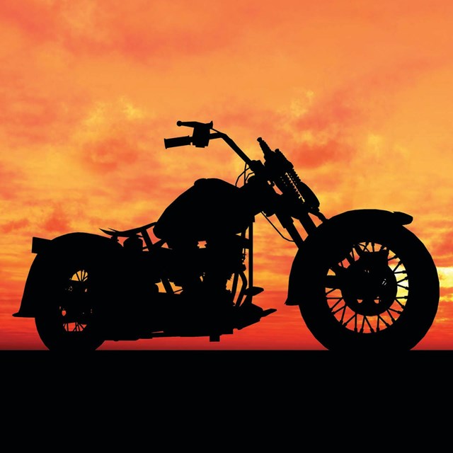 A black silhouette of a motorcycle stands in contrast to a bright orange and red sunset.