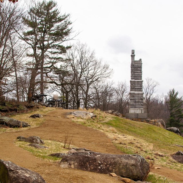 Dirt path leading through boulders up to two stone monuments and two cannons.