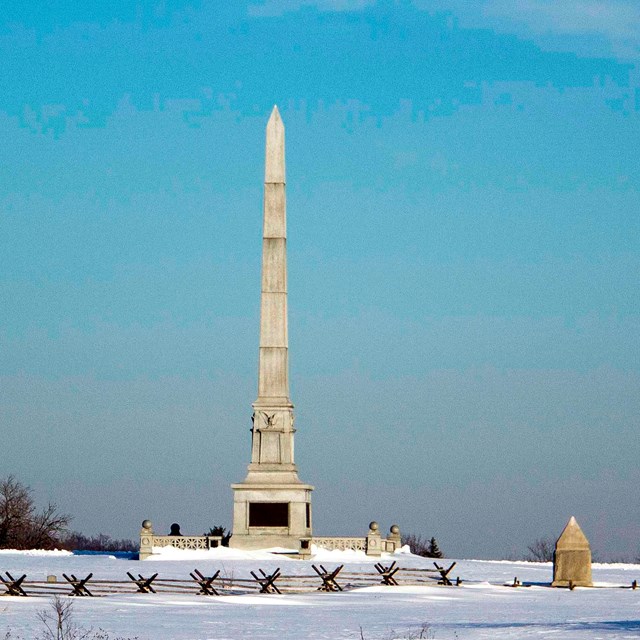 A large stone monument in a snow-covered field with various smaller monuments in the area.