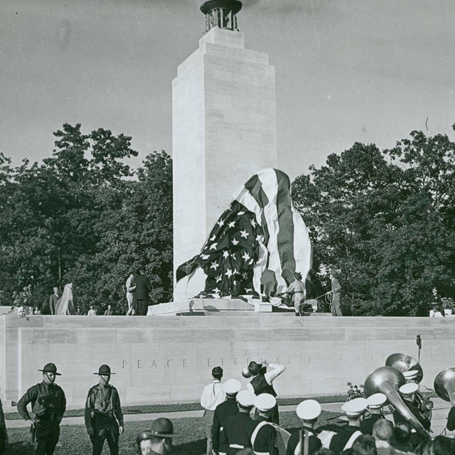 A black and white photo of a band in front of a large white stone monument unveiling.