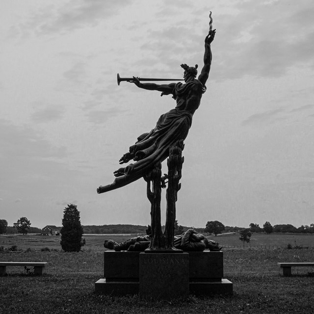 A black and white photo of a monument with a person blowing a instrument. 