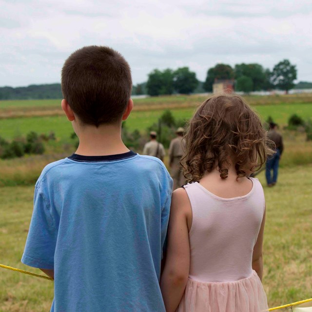 A boy and a girl watch an artillery living history demonstration. 