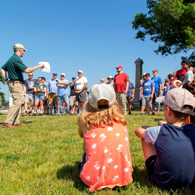 Three children watch a park volunteer give a talk outside.