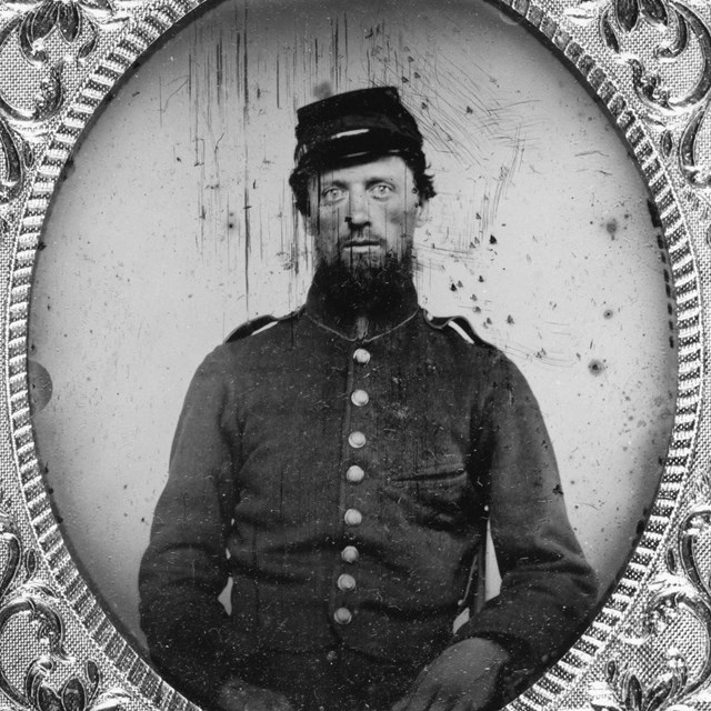 A black and white photo of a soldier in uniform set in an ornate oval frame.
