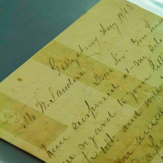 A hand written letter on yellowed paper with faint lines lays on a table.