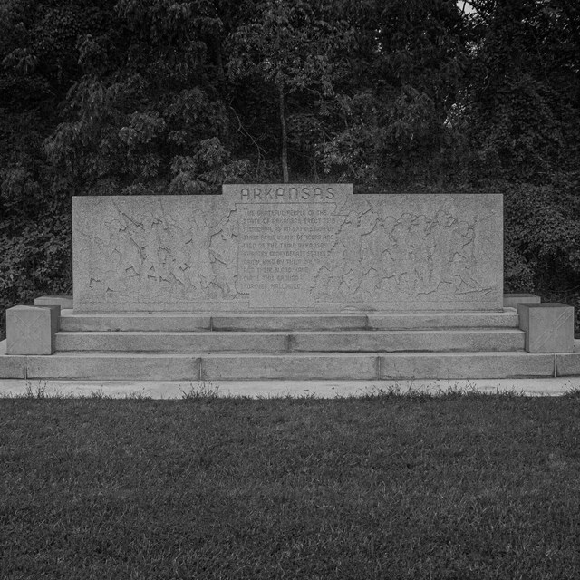 A black ad white photo of a stone monument with with the silhouettes of soldiers on it.