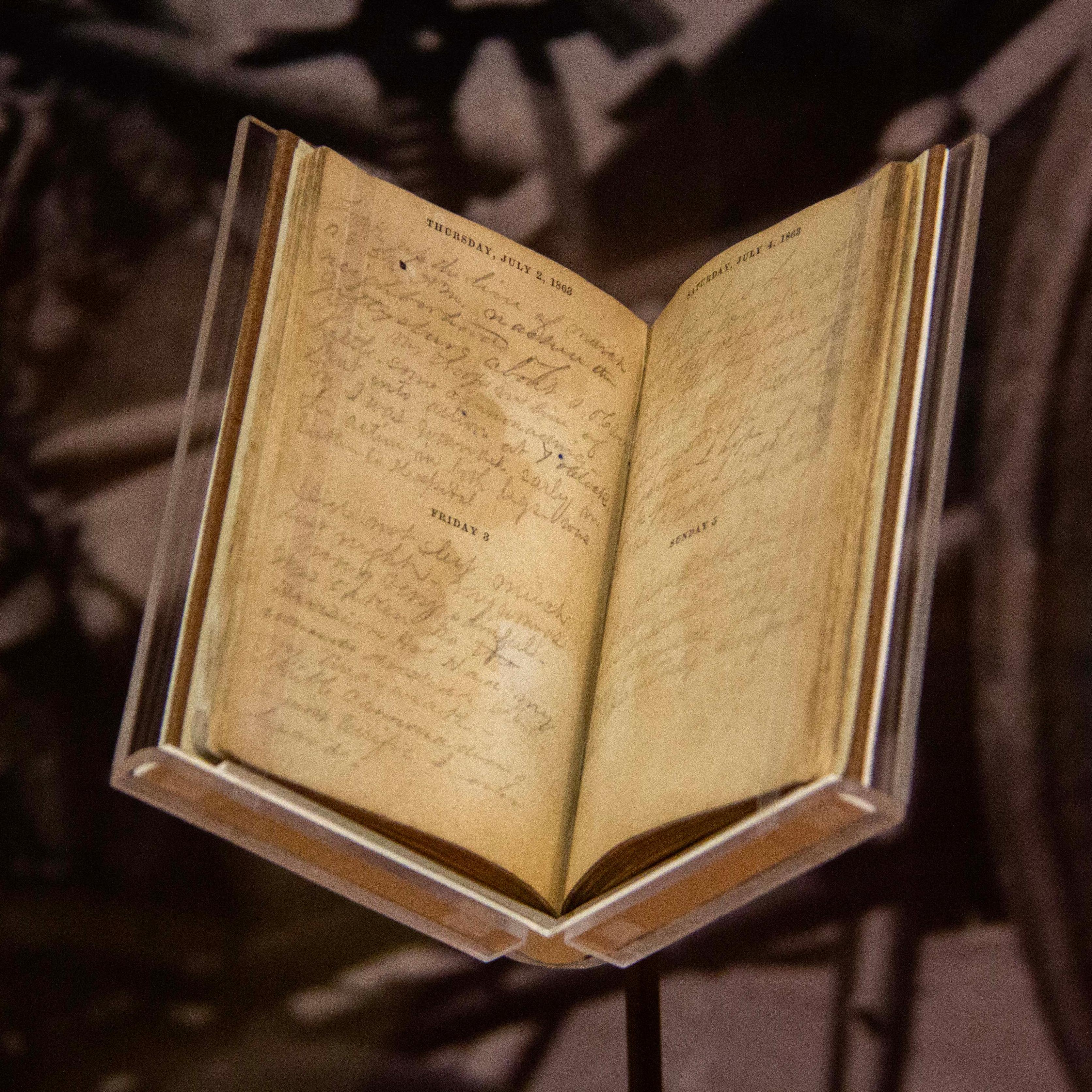 An antique book with yellow faded pages sits open. Inside is faint pencil cursive writing.
