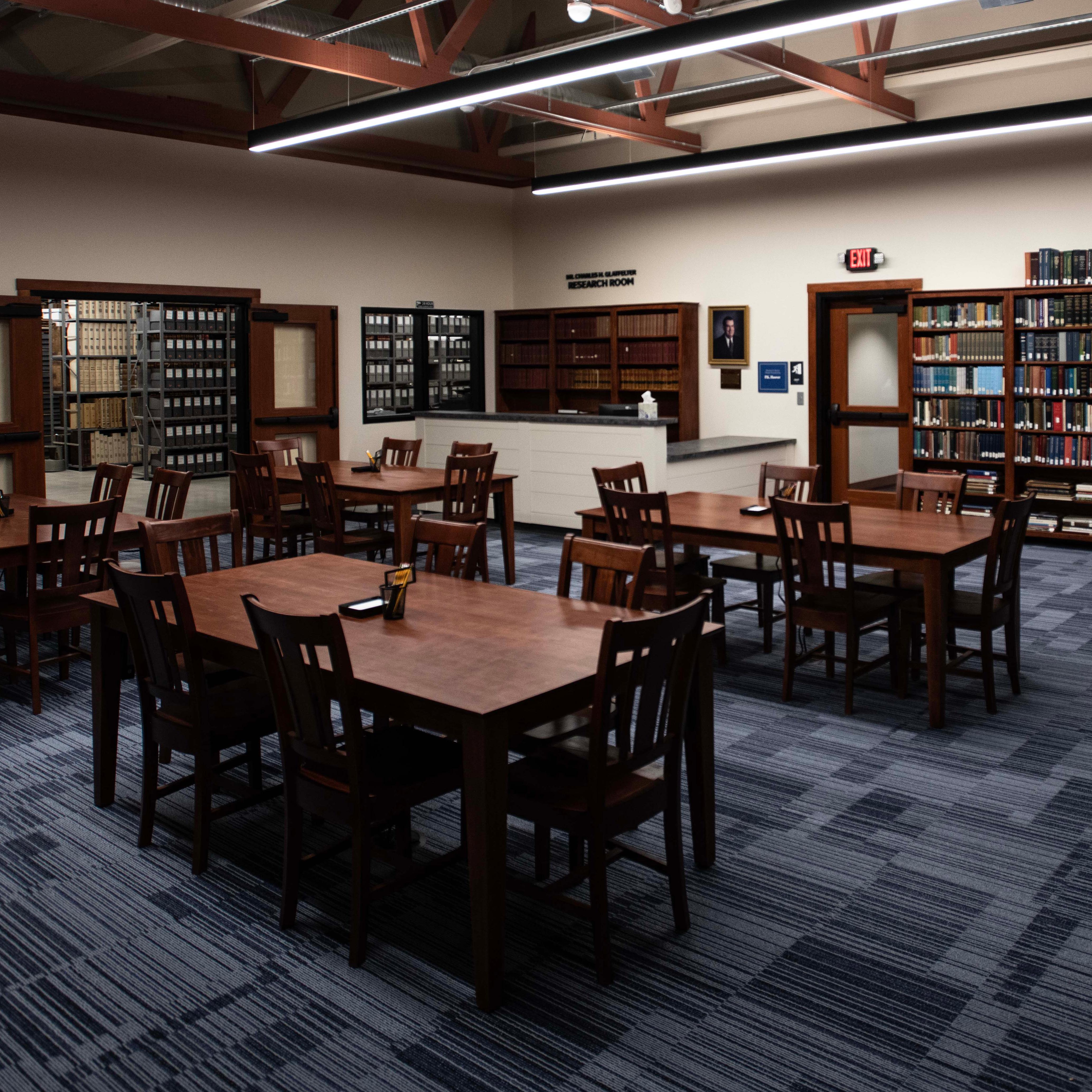 A research room with two large tables with multiple chairs and lots of bookcases along the walls.