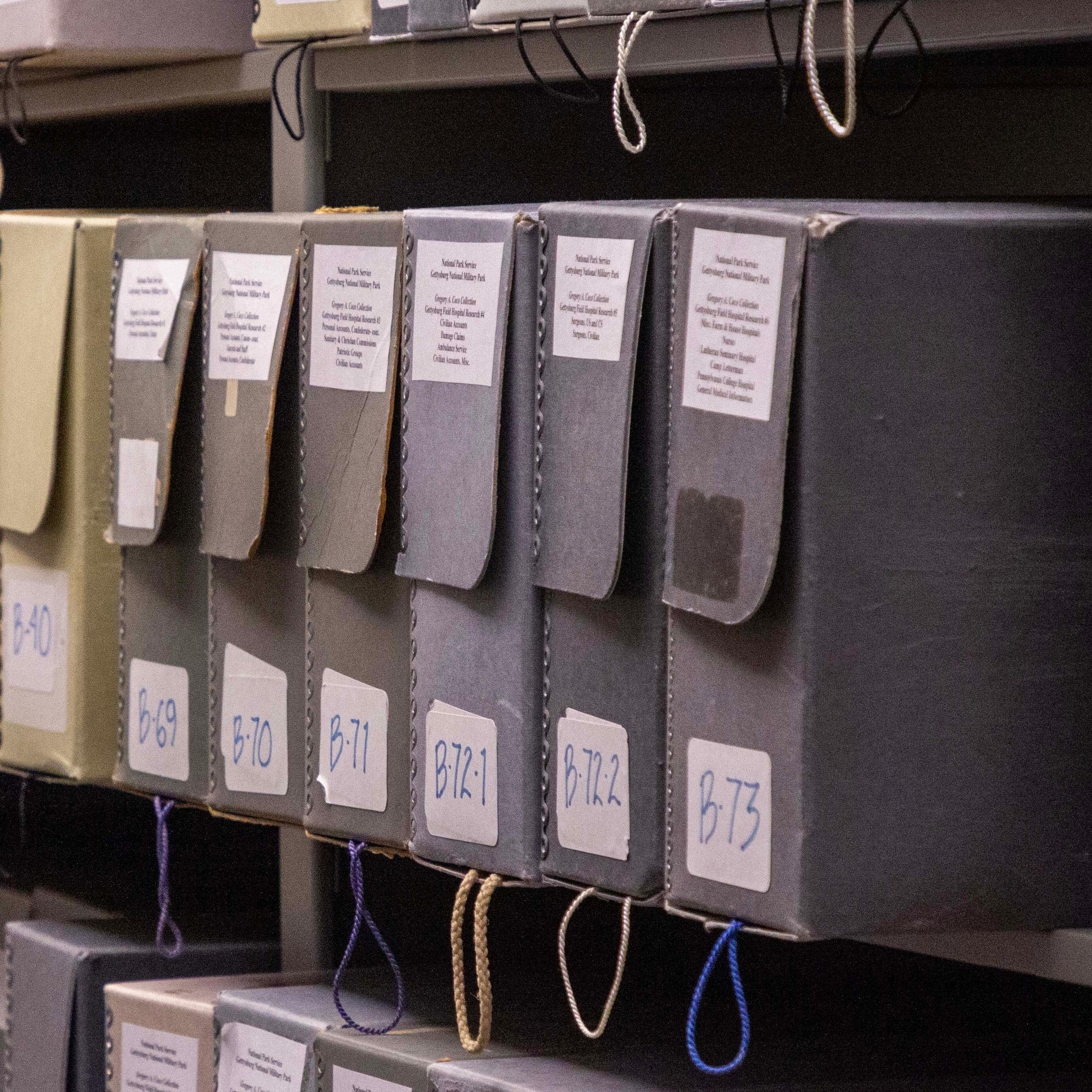 A row of grey, brown, and cream colored boxes with white labels sit on grey shelves.