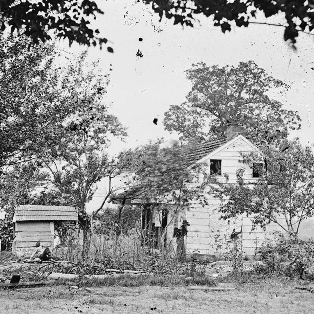 A black and white photo of a farm house and barn, a few people standing near