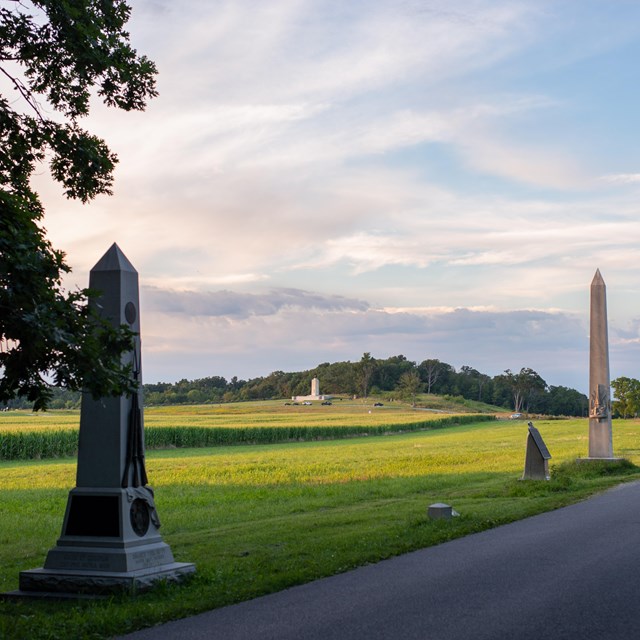 A row of monuments, statues, plaques, and obelisks line the left side of a road.