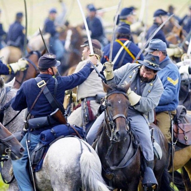 A scene of Civil War cavalry soldiers reenacting a fight scene while on horseback.