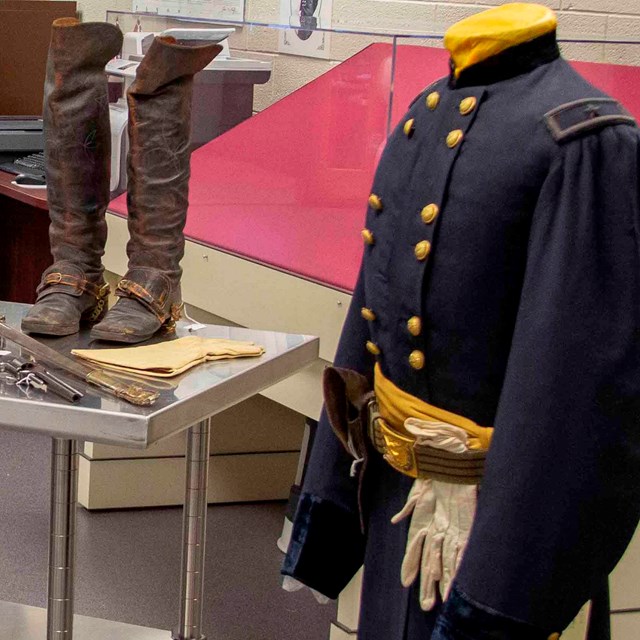 A number of Civil War artifacts sit on a metal table and a blue Union uniform stands to the right.