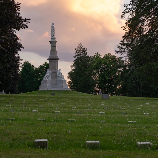 Rows of stone grave markers in front of a tall white monument.