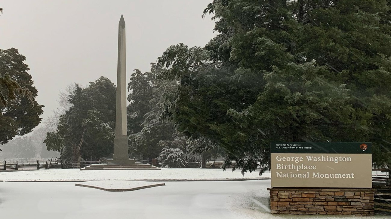 White obelisk, surrounded by snow covered landscape and road. 