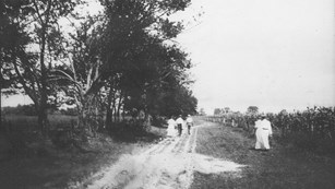 1930 black and white photo of men and women walking on sandy road
