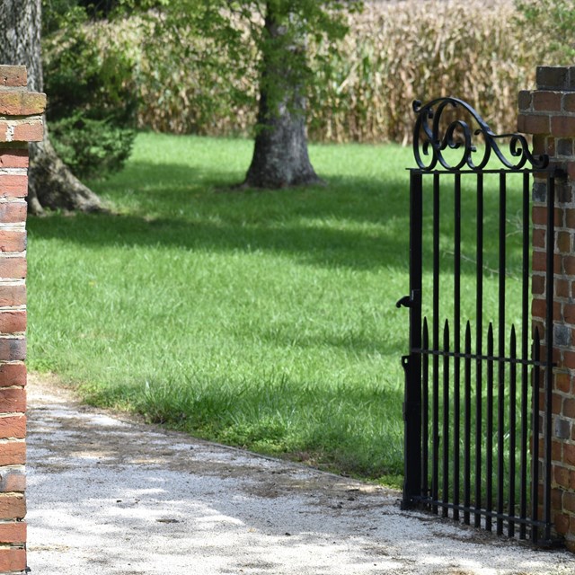 metal gate opening to loose gravel path surrounded by brick fence