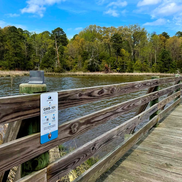 A bridge stretching over water, a phone holder and a sign to the left on the bridge railing