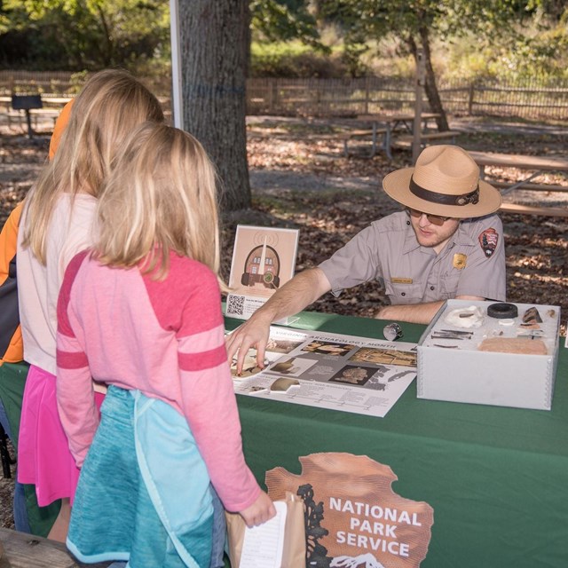 Kids interacting with a park ranger at a booth with pamphlets.