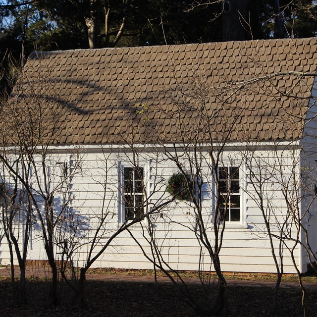 Exterior image of the shop with one door and two windows and a wreath between the two