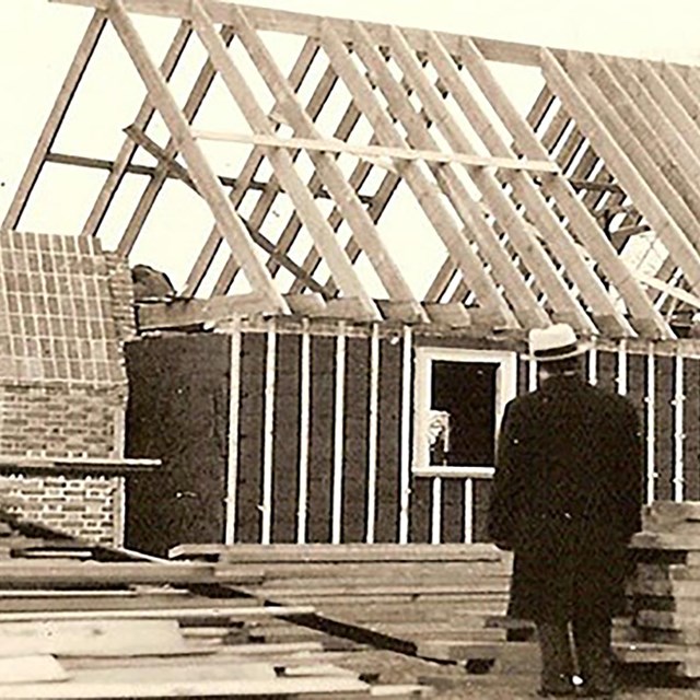 sepia photo of the construction of the memorial house with a man looking at the house.