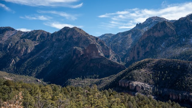 A steep Canyon with mountains on the opposite side, some of the northern facing slopes have snow.