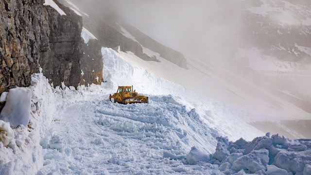 A tractor plows snow in the mountains. 