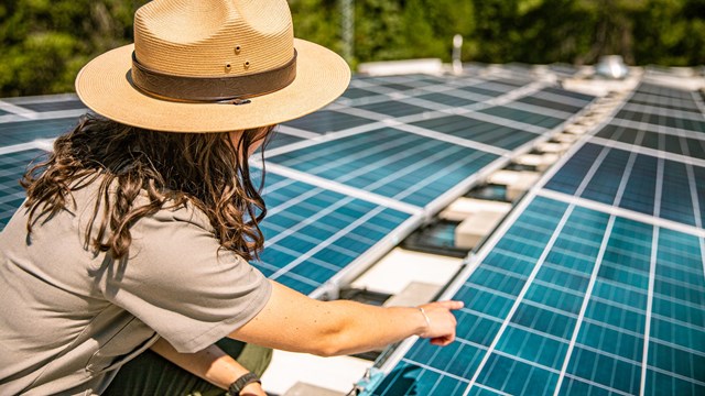 A park ranger points to solar panels. 