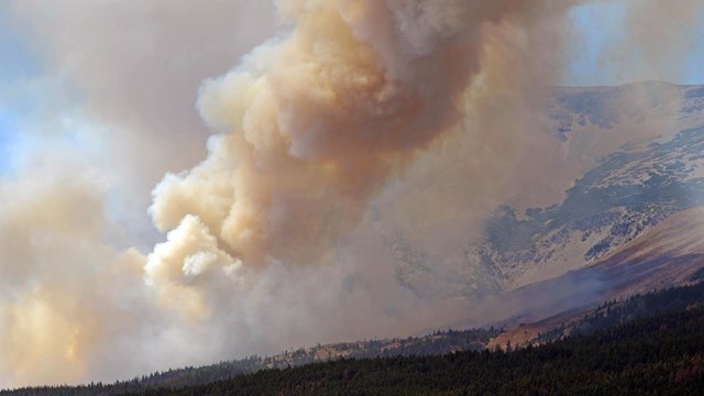 Smoke and large plume billow over mountain ridge