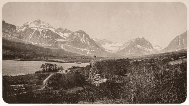 black and white of an oil well in the foreground and Grinnell Glacier behind it