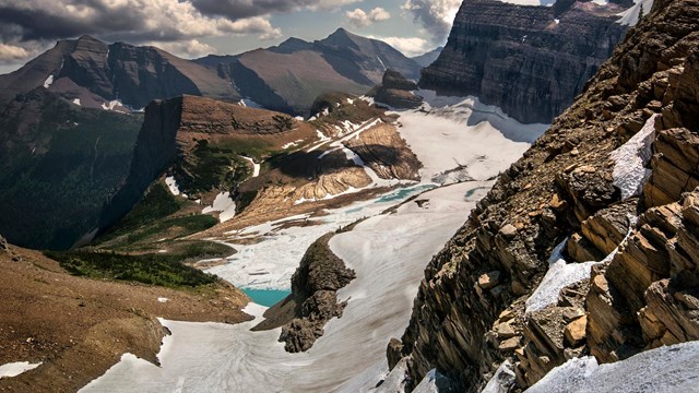 looking down on snow covered glacier, terraces, and icy teal lake
