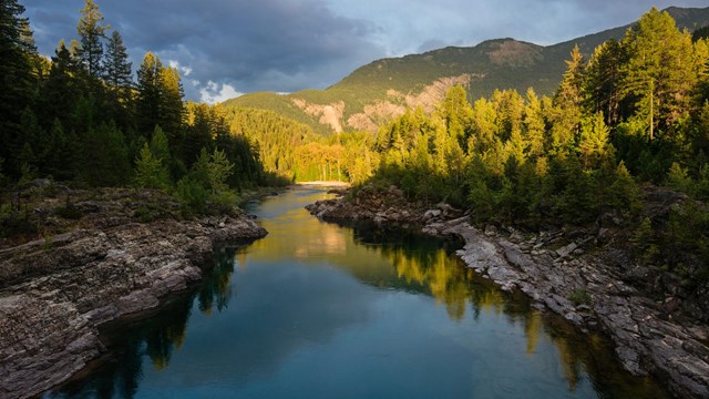 River with rocky banks snakes through a sunset-lit forest