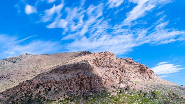 wispy clouds and blue skies over a mountain