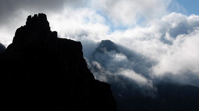 clouds creep over silhouetted mountain peaks