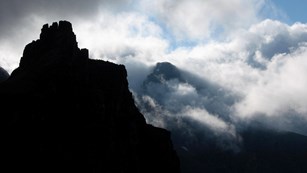 clouds creep over silhouetted mountain peaks