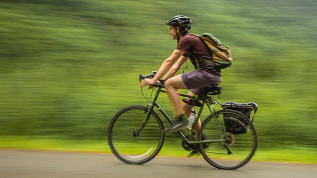 A biker wearing a backpack and helmet speeds by.