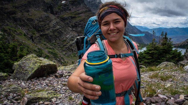 Person on trail holds up reusable water bottle.