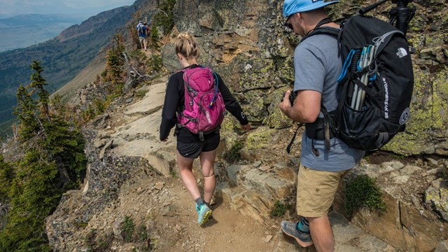 Two people walking down a mountain trail. 